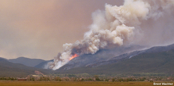 Left-right oriented smoke plume riding up the slope of a mountain.