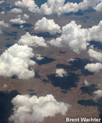 Areal photo of scattered clouds casting shadows on the earth.